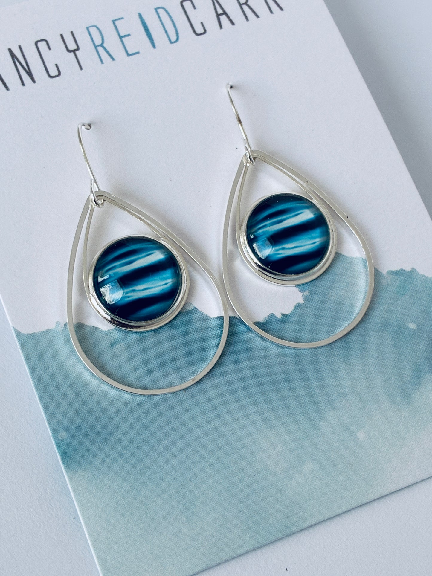 Teardrop-shaped earrings with blue and silver design on a branded card